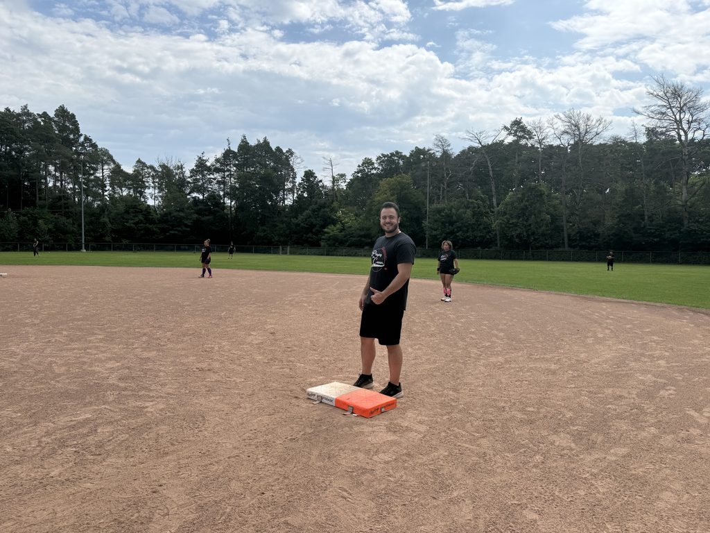 A man smiling at first base in a baseball diamond. 
