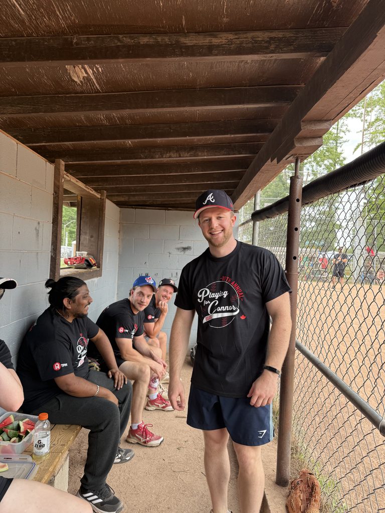 A group of men in a baseball dugout smiling. 
