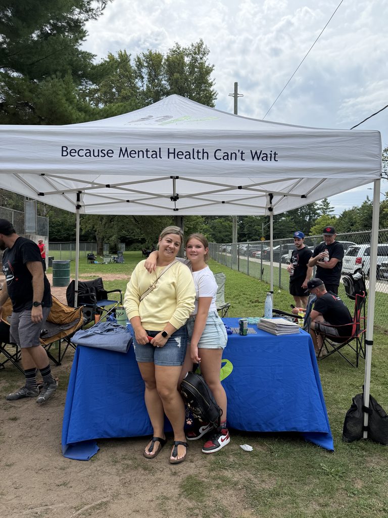 A woman and a teen smiling in front of  a New Path branded tent. 