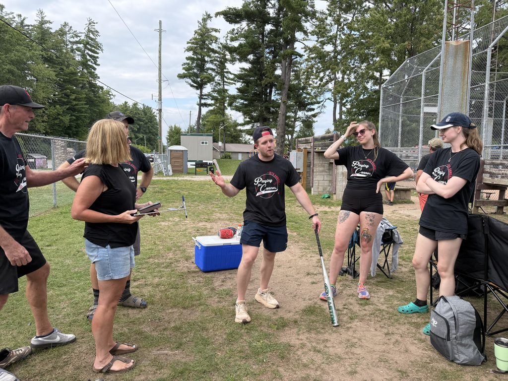 A person holding a bat and talking as others look at him