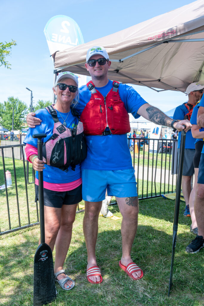 A woman and a man wearing life jackets smiling and holding paddles