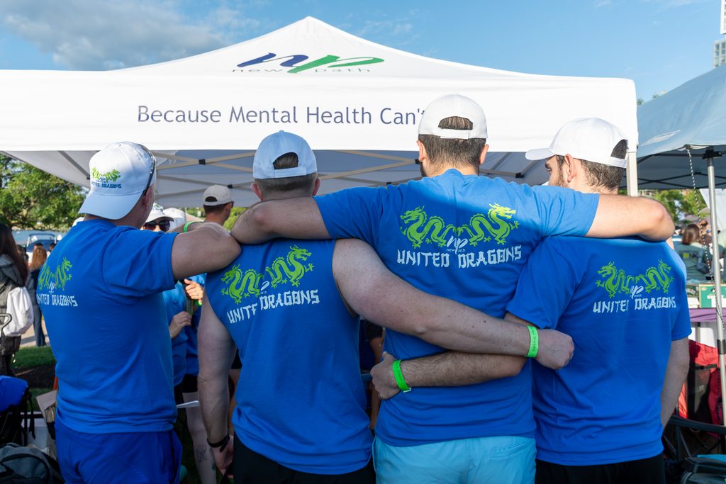 Picture of four people's back holding onto eachothers waists wearing New Path United Dragons t-shirts