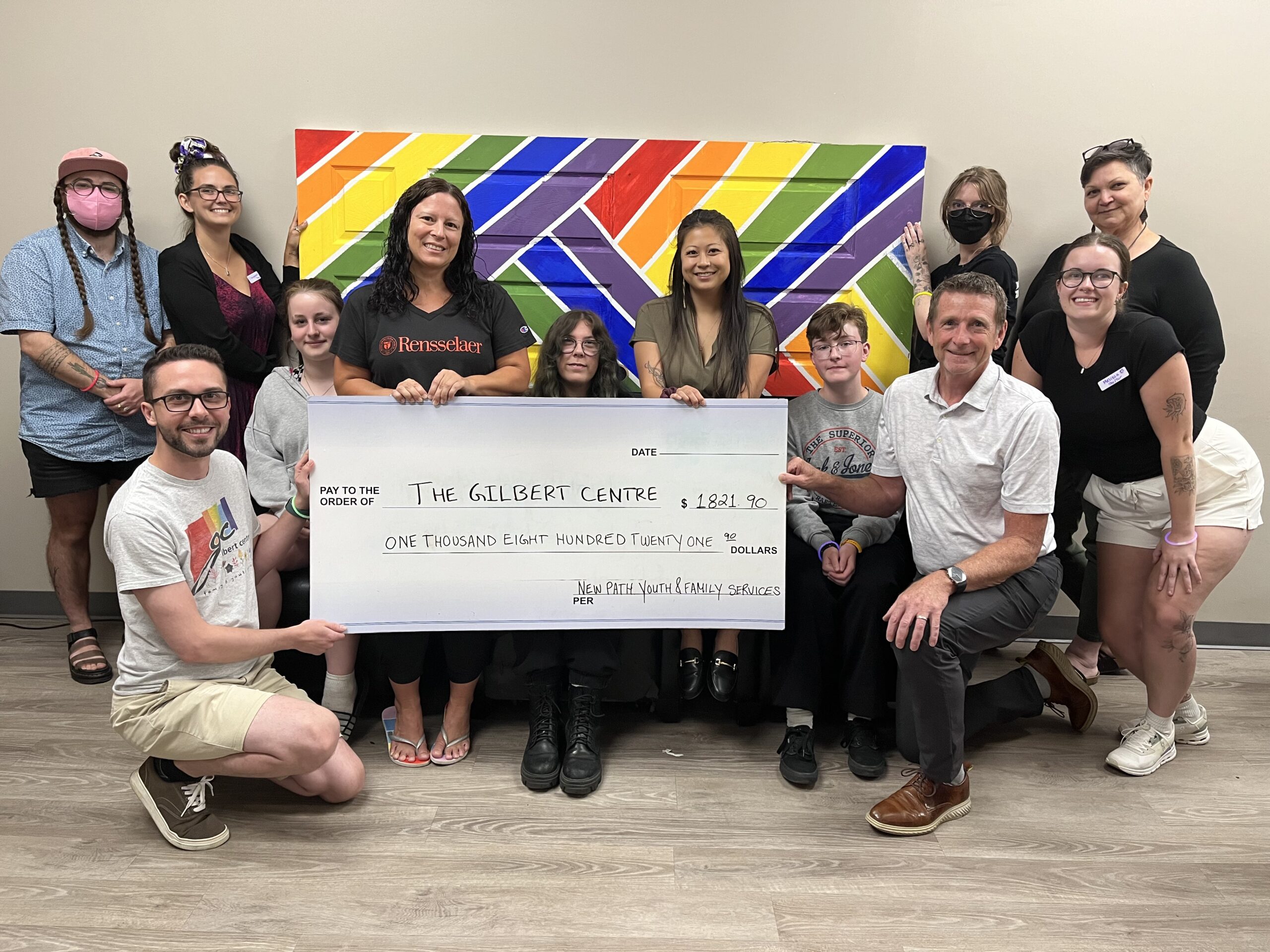 Youth organizers and staff from New Path and the Gilbert Centre celebrate the receipt of over $1800 from the second annual youth-led PRIDE BBQ held at Sunnidale Park. Attendance at this year’s event increased as did the donation amount from the community. All proceeds from the event support 2S-LGBTQ+ programming at the Gilbert Centre. Bottom left to right are: Dale Boyle, Executive Director of the Gilbert Centre; Jim Harris, CEO of New Path. Middle left to right are: Jenny Johnston, Youth Committee Member; Daneen Ens, Care and Treatment Worker at New Path and event organizer; Cemya Nugent, Youth Committee Member; Jaclyn Ng Man Chuen, Equity, Diversity and Inclusion Implementation Lead at New Path; Conner Klages, Youth Committee Member; Mellissa Bennett, Placement Student at the Gilbert Centre. Top left to right are: Ellis Greenberg, Queer & Trans Program Manager at the Gilbert Centre; Champagne Thomson, Community Outreach and Fundraising Senior Manager at the Gilbert Centre; Kat Bransfield, Community Worker at the Gilbert Centre; Dani Chase, Care Coordinator at the Gilbert Centre.