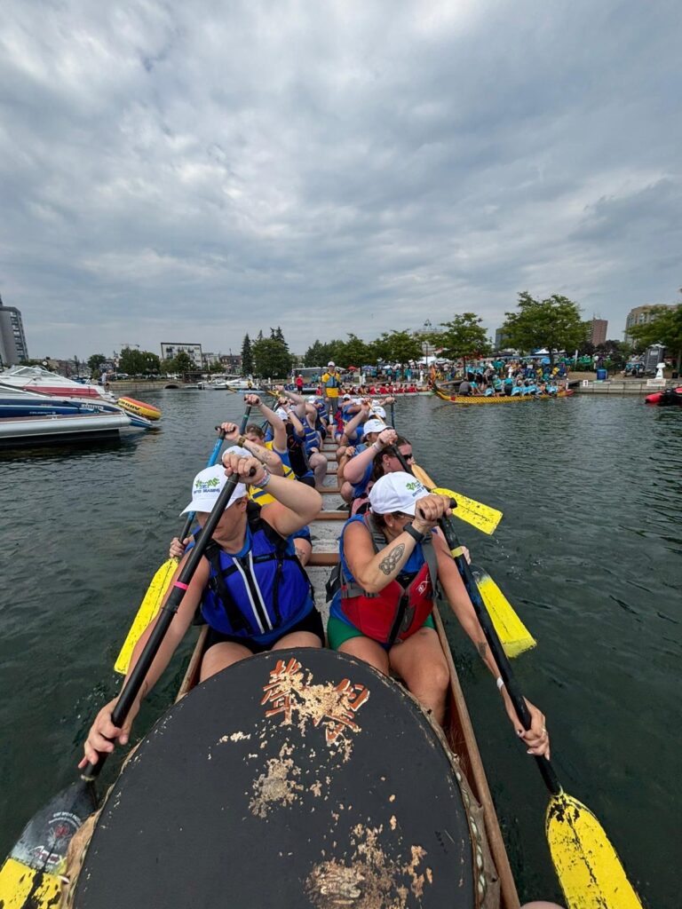 Group of people wearing life jackets and matching white hats paddling in a dragon boat.