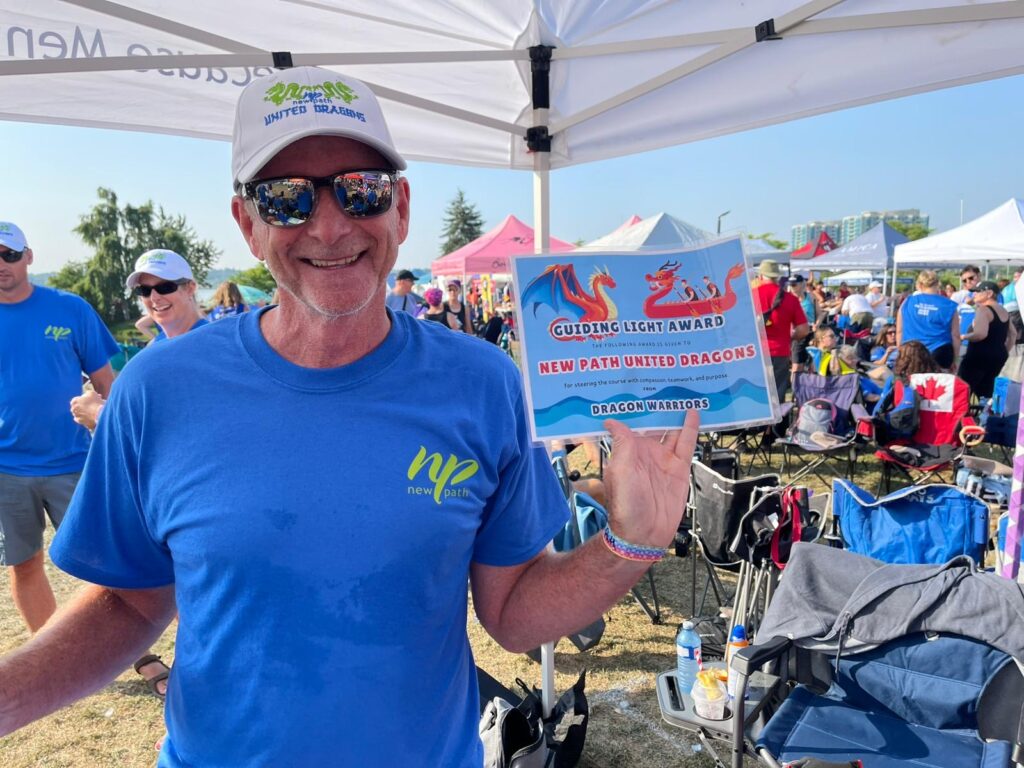 Picture of a man smiling holding a certificate of accomplishment for a dragon boat race.