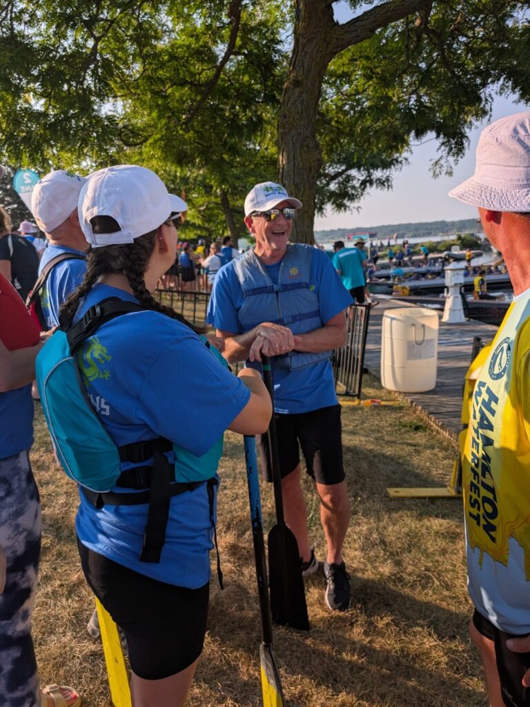 Picture of people in life jackets holding paddles talking with water in the background.