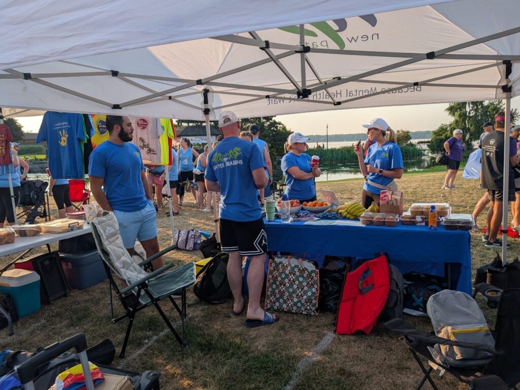 Group of people wearing matching white hats and blue New Path United Dragons t-shirts standing under a tent in front of and behind a table with food on it.